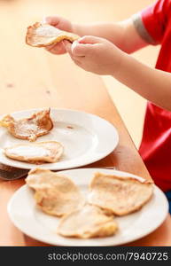 Little boy eating fried apple in pancake dough or apple fritters pancakes with icing sugar at home