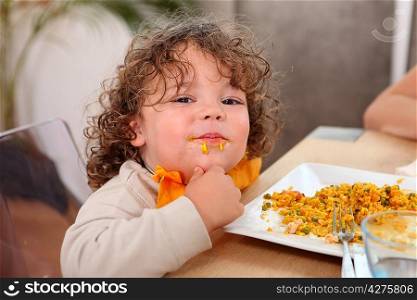 Little boy eating rice at kitchen table