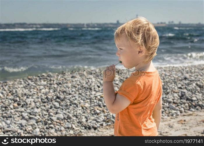 Little boy eats lollipop is on seashore in the summer, Denmark