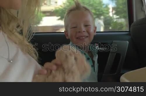 Little boy enjoying car ride with teddy bear and mom. Kid giving hugs to favorite toy and mother embracing him