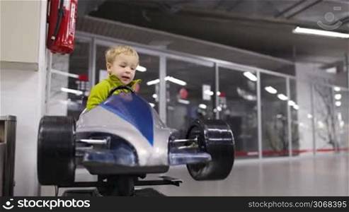 Little boy enjoying himself driving an elevated model racing car in an indoor mall or car showroom