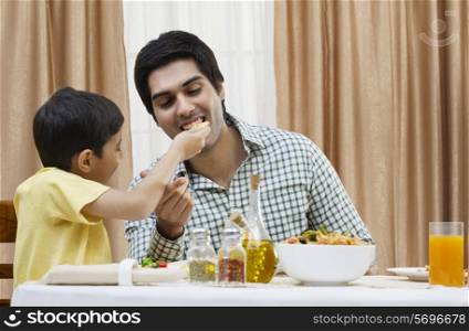 Little boy feeding piece of pizza to father at restaurant
