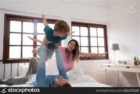 Little boy flying with dad using his legs to help him fly high off the floor of his bed in the bedroom.