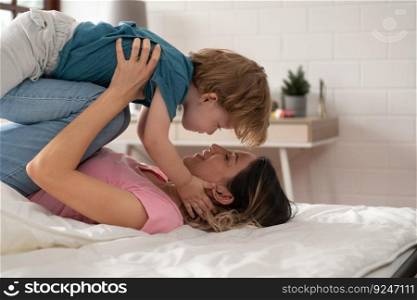 Little boy flying with mom using her legs to help him fly high off the floor of his bed in the bedroom.