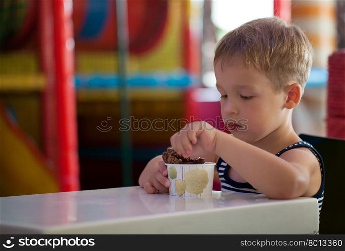 Little boy having tasty chocolate ice cream sitting at the table in game room