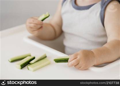 little boy highchair holding cucumber pieces
