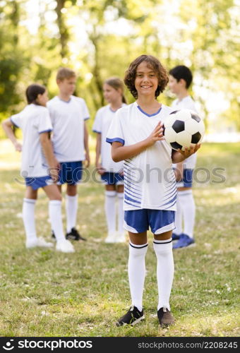 little boy holding football outside other kids