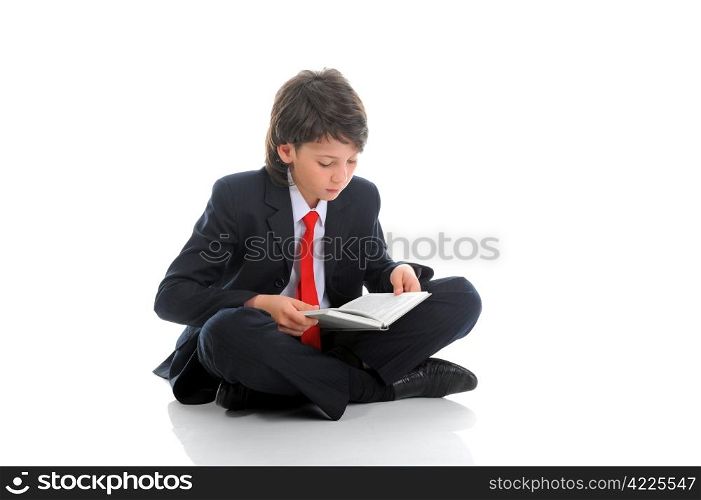 little boy in a business suit reading a book sitting on the floor. Isolated on white background