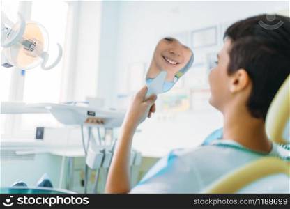 Little boy in a dental chair looking in the mirror at his teeth, pediatric dentistry, children stomatology