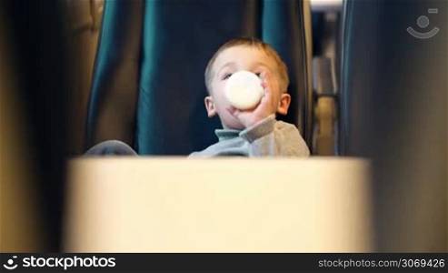 Little boy in express train drinking milk from the bottle. View between two seats