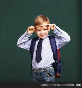 little Boy in eyeglasses with big backpack. School, kid, rucksack. Cheerful smiling little kid against chalkboard. Looking at camera. School concept. Back to School