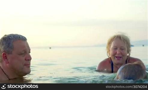 Little boy in goggles is in the sea with his grandparents, he is swimming underwater between them.