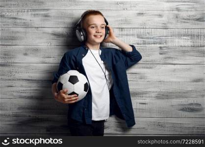 Little boy in headphones holds ball in studio. Children and gadgets, kid isolated on wooden background, child emotion, schoolboy photo session. Little boy in headphones holds ball in studio