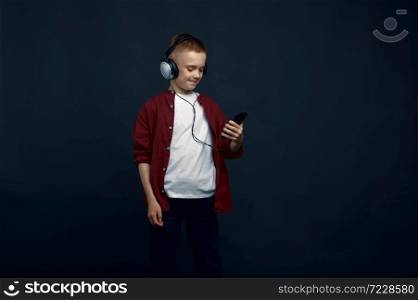 Little boy in headphones listen to music in studio. Children and gadget, kid isolated on dark background, child emotion. Little boy in headphones listen to music in studio