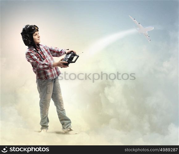 Little boy in pilot&rsquo;s hat. Image of little boy in pilots helmet playing with toy radiocontrolled airplane against clouds background