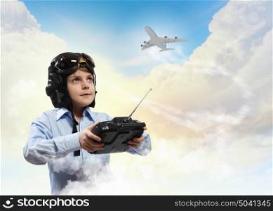 Little boy in pilot&rsquo;s hat. Image of little boy in pilots helmet playing with toy radiocontrolled airplane against clouds background