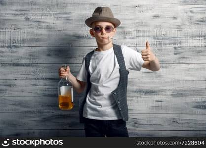 Little boy in stylish hat holds bottle in studio. Kid isolated on wooden background, child fashion, schoolboy photo session. Little boy in stylish hat holds bottle