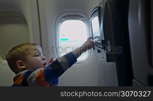 Little boy in the airplane touching seat monitor with finger