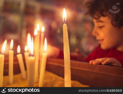 Little boy in the church on Easter, puts a candle to prays to God, enjoying happy religious holiday, good peaceful atmosphere in holy place. Little boy in the church on Easter