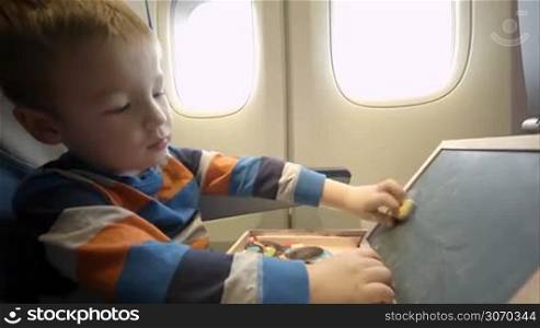 Little boy in the plane wiping the board of his wooden box with magnets and closing it