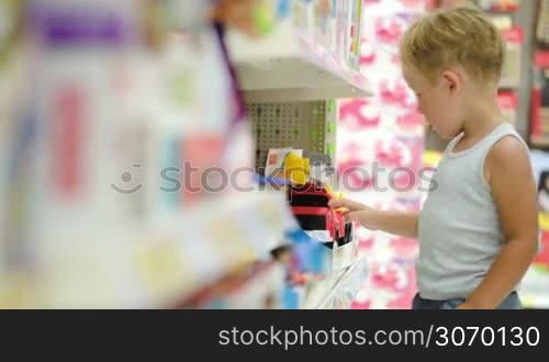 Little boy in the toy shop looking at car on the shelf and playing with it