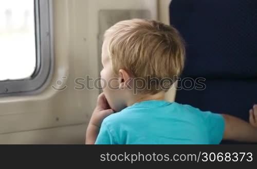 Little boy in the train looking out the window, mother pointing somewhere and talking.
