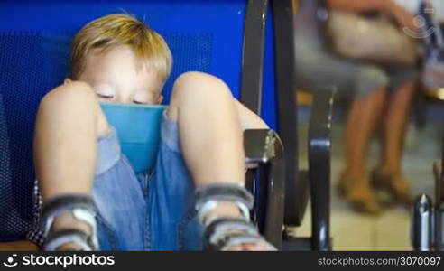 Little boy in waiting room using tablet computer sitting on the chair with his feet on it