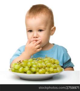 Little boy is eating grapes, isolated over white