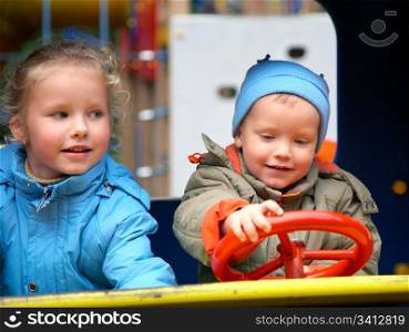 Little boy is learning to drive on the pleasure-ground and his sister
