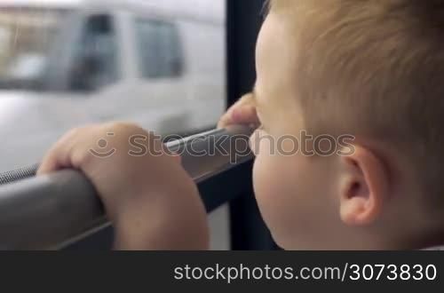 Little boy is looking out the window of moving bus. He is pointing at something interesting and smiling.