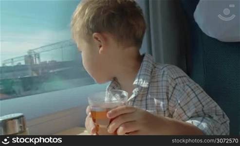 Little boy is sitting in coach by the window. He&acute;s drinking tea and talking to his parents emotionally.