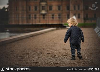 Little boy is walking on a dirt road to an old building