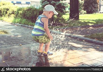 Little boy jumping in puddle. Summertime playground