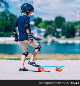 Little boy learning skateborading in park by the lake
