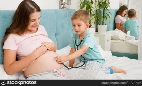 Little boy listening to mothers pregnant big belly with stethoscope. Concept of healthcare and medical examination during pregnancy.. Little boy listening to mothers pregnant big belly with stethoscope. Concept of healthcare and medical examination during pregnancy