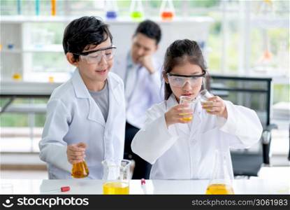 Little boy look to little girl pour some color chemical to flask in laboratory class room. Concept of good practice and education of science for children support their learning.