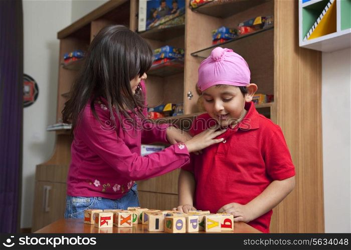 Little boy looking at wooden toy blocks while standing with sister