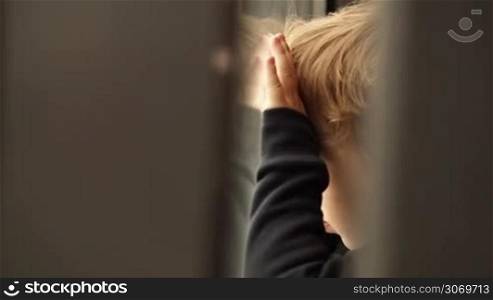 Little boy looking out of the window with his face and hands close to it and reflected in the glass