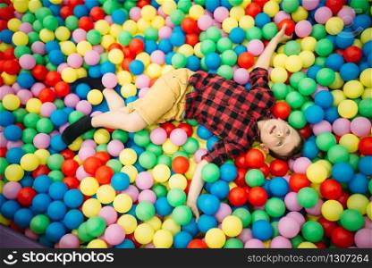 Little boy lying in a pile of colorful inflatable balloons in childrens entertainment center. Happy childhood. Little boy lying in a pile of colorful balloons