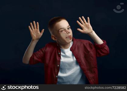 Little boy makes face leaning against the glass in studio. Happy childhood, children having fun, funny kid isolated on dark background, child emotion. Little boy makes face leaning against the glass