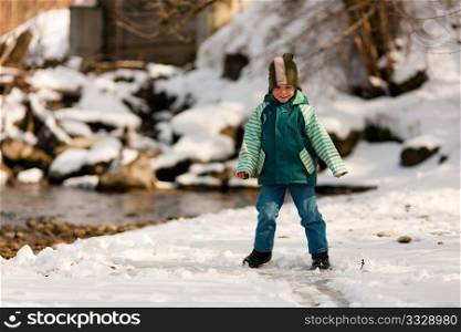 Little boy on a walk along a riverbank in winter; the child is standing on the ice