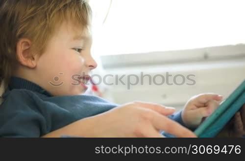 Little boy on mothers lap in the train using tablet PC held by mom