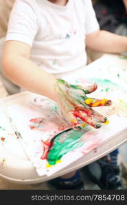 Little boy painting with colorful finger-paints. Colored hand and abstract painting in focus