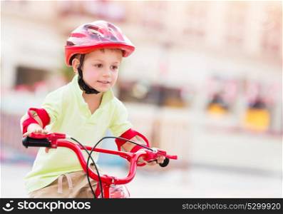 Little boy playing outdoors, cute cheerful child having fun in summer camp, nice kid riding on red stylish bicycle on blur urban background, enjoying carefree summer holidays