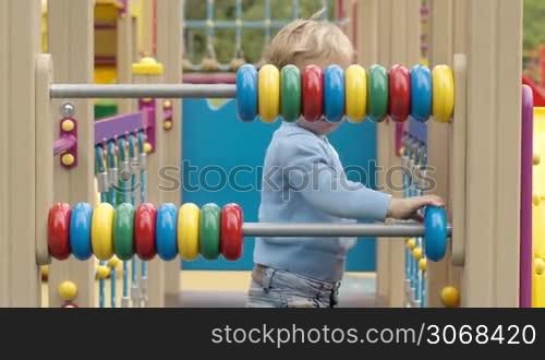 Little boy playing with an abacus with colourful rings on two bars in a childs playground as he learns to count