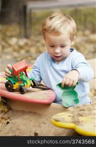 Little boy playing with toy tractor rolling it on the bench. Having fun outdoors.