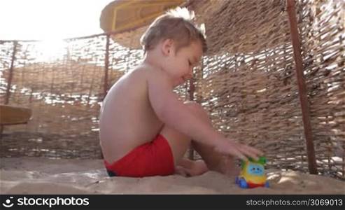 Little boy playing with toy truck on the beach on a hot summer day