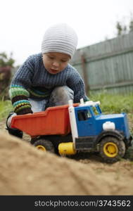 Little boy playing with toy truck rolling it on the sand. Having fun outdoors.