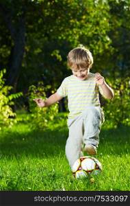 Little boy plays with a football in a summer garden