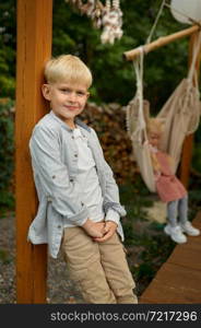 Little boy poses on motorhome terrace, summer camping. Family with children travel in camp car, nature and forest on background. Campsite adventure, travelling lifestyle, smiling kid camper. Little boy poses on motorhome terrace, camping